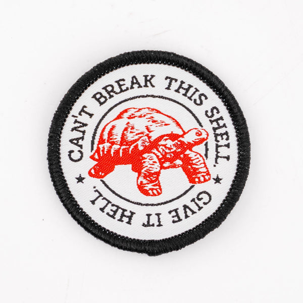 White patch with black border, "Can't Break this Shell. Give it Hell." woven over white with a red tortoise.